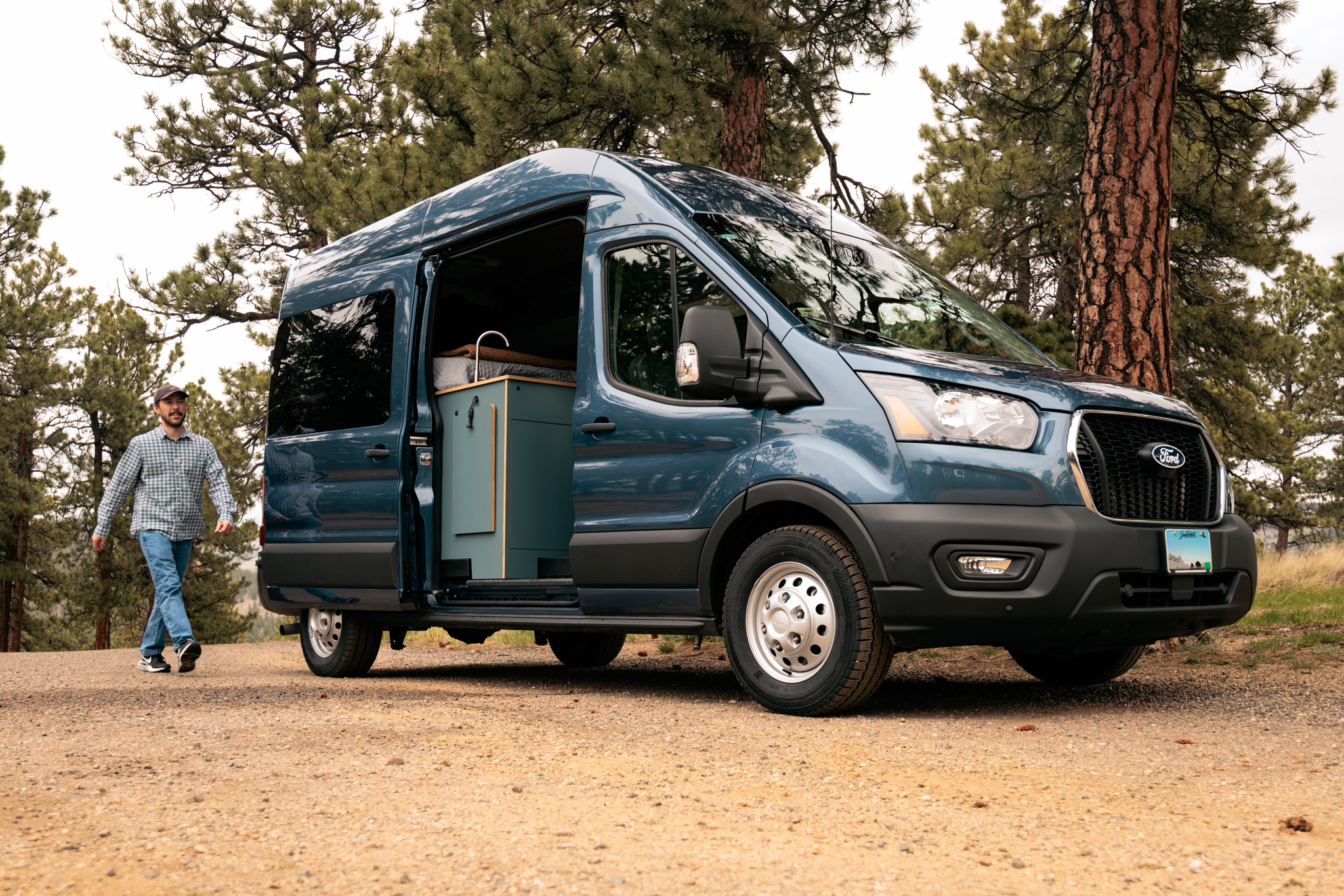 Blue Ford Transit Timber Rambler parked among pine trees
