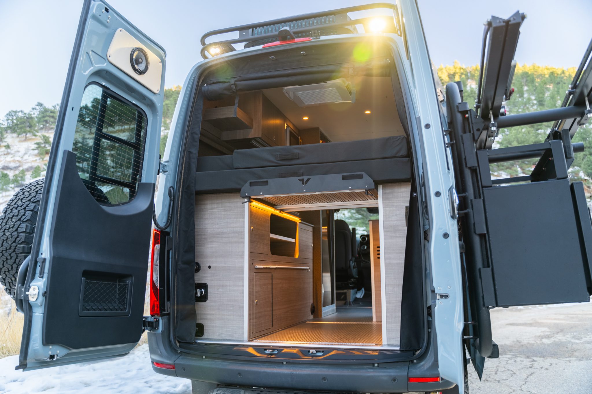 Rear doors open on the raised bed and the Elm laminate cabinetry, with the rear door ladder and tire combo