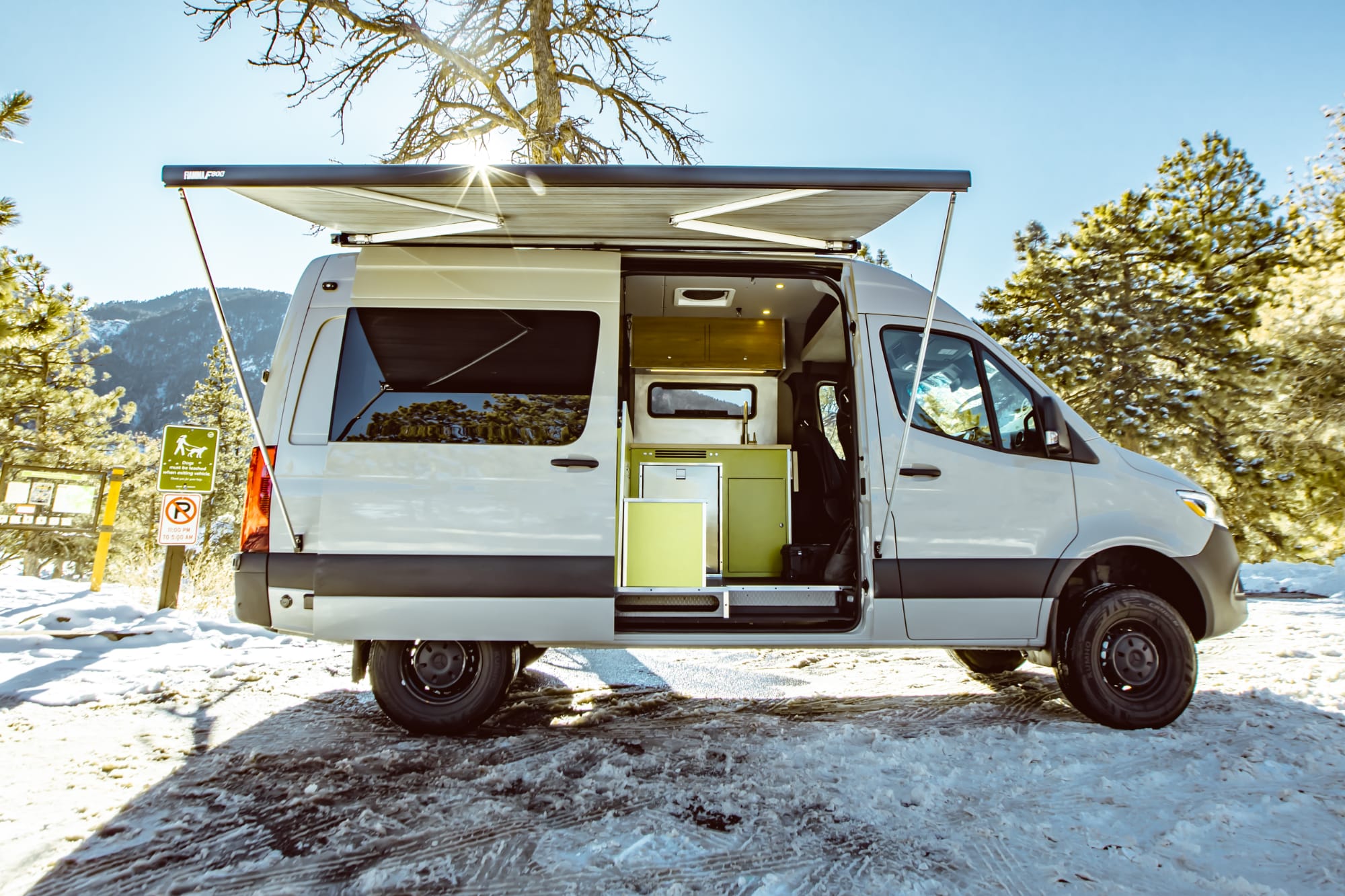 A white Mercedes Sprinter camper van with the side door open and the awning retracted.