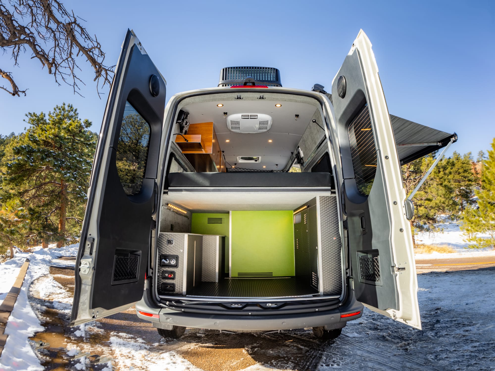 A view of a camper van from the rear with the two rear doors open. You can see the bed from the back and the spray down shower.