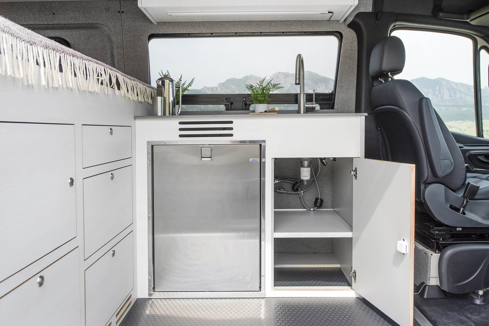 The Kronos campr van's galley with a stainless steel fridge and the cabinet door open